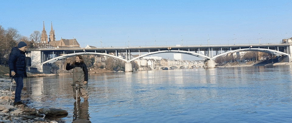 Zwei Personen stehen am Rhein und nehmen Wasserproben
